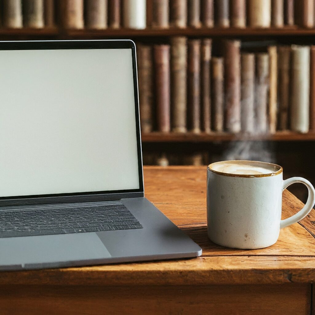 An open laptop and nice warm coffee sitting in an old library, just waiting to help you with your writers block